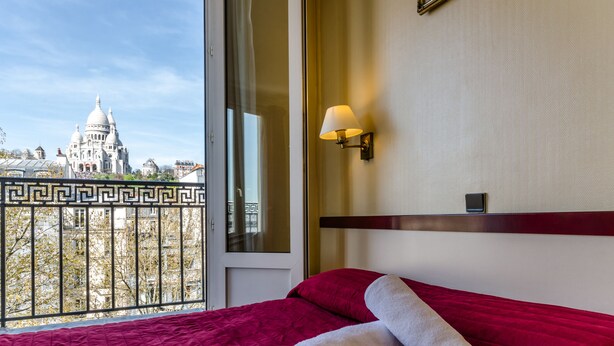 Habitación de hotel con una ventana grande, una cama con colcha roja, una toalla blanca y vistas a un edificio con cúpula.