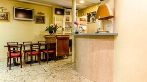 Un área de recepción con un mostrador de madera, un televisor montado en la pared y varias sillas dispuestas para los huéspedes.