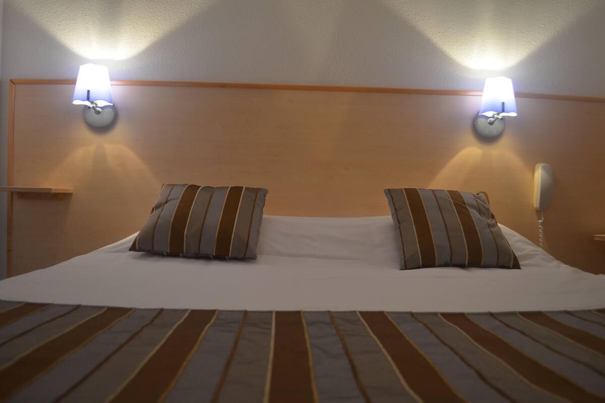 A neatly made bed with striped bedding and two pillows, two wall-mounted lamps, and a telephone on the right side.
