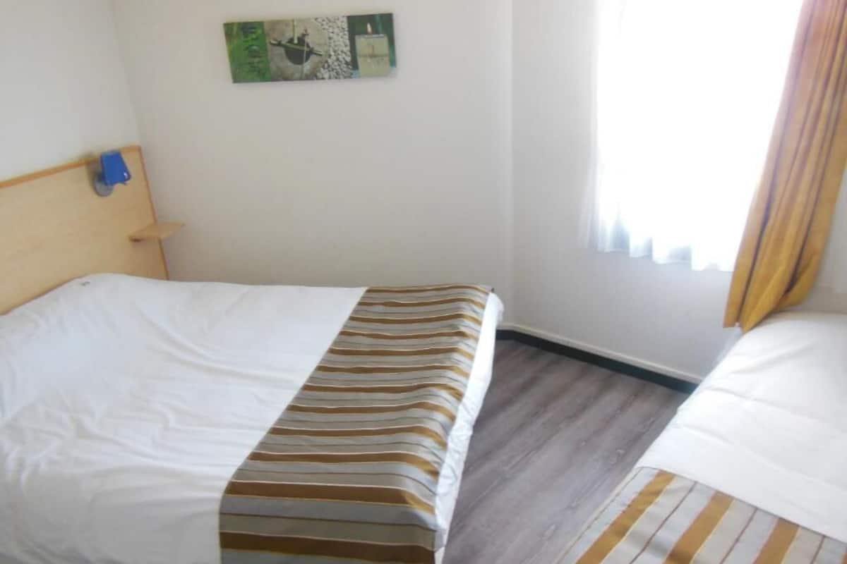 A hotel room with a bed, a headboard, a wall-mounted artwork, and a window with curtains.