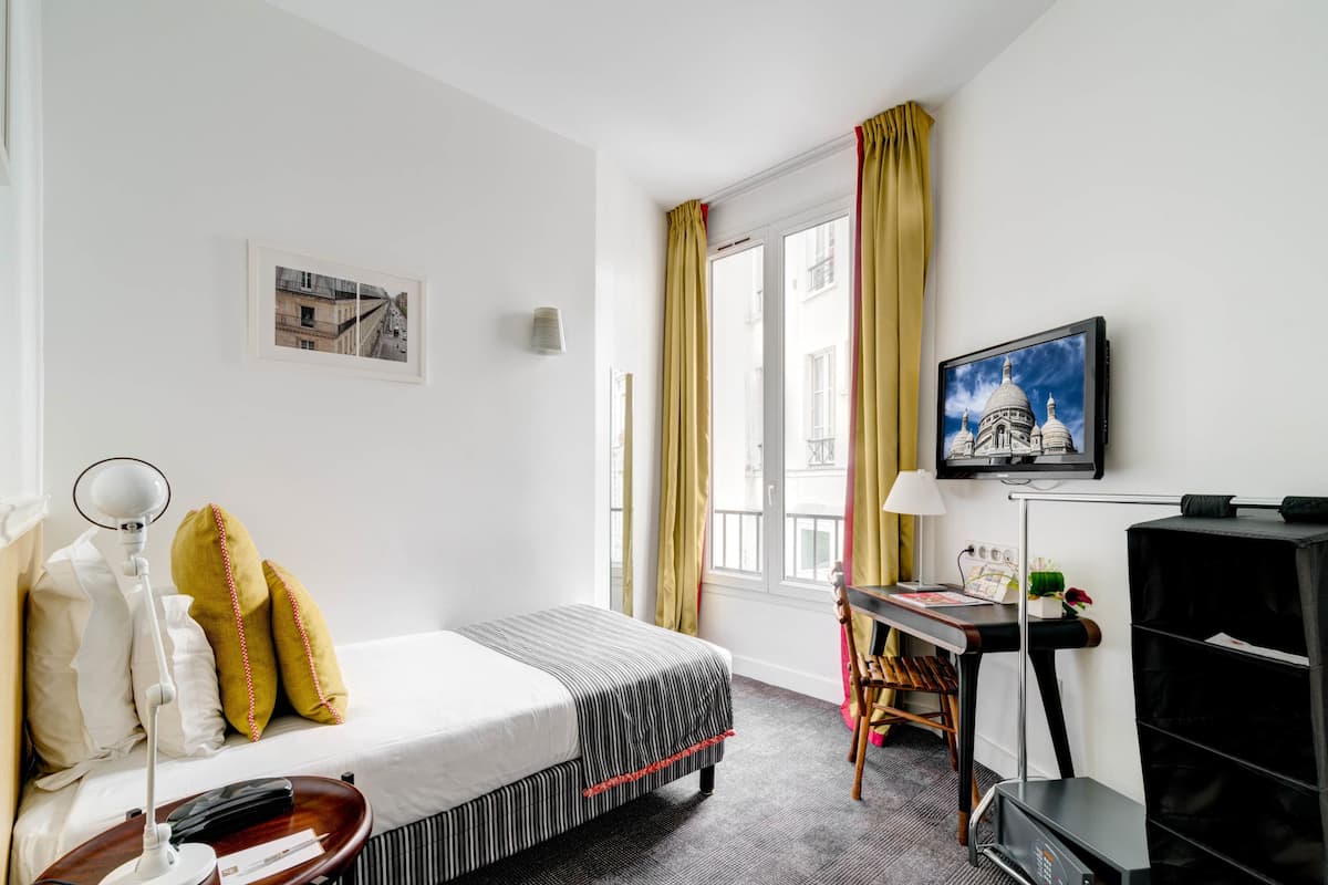 Ein Hotelzimmer mit Bett, Schreibtisch, Stuhl, Fernseher und einem Fenster mit Vorhängen.