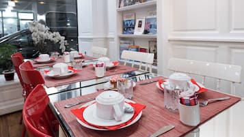 Een eetgedeelte met een glazen tafel, rode stoelen, witte borden en een witte theepot.