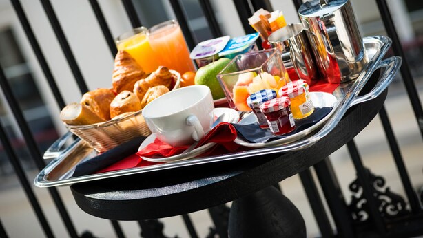 Bandeja de desayuno con croissants, una taza, un vaso de zumo de naranja y una termo en un balcón.