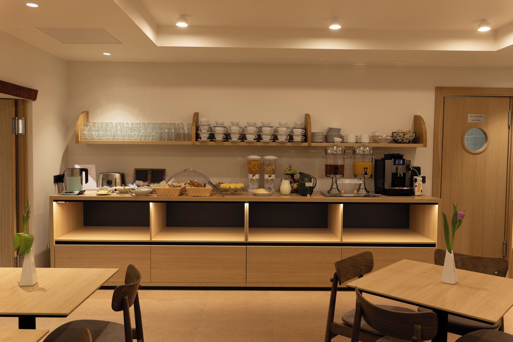 A modern hotel room with a breakfast bar, wooden furniture, and a coffee machine.
