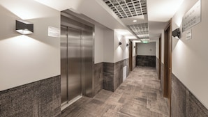 A hallway with a metallic elevator, a wall-mounted light, and a sign indicating the floor level. - IVOLITA Vilnius Hotel (Vilnius)