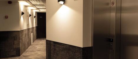 A hotel corridor with a carpeted floor, a wall-mounted light, and an elevator with a digital display.