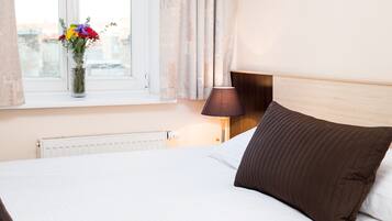A hotel room with a bed, a window with curtains, a vase with flowers, and a bedside lamp.