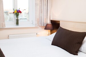 A hotel room with a bed, a window with curtains, a vase with flowers, and a bedside lamp.
