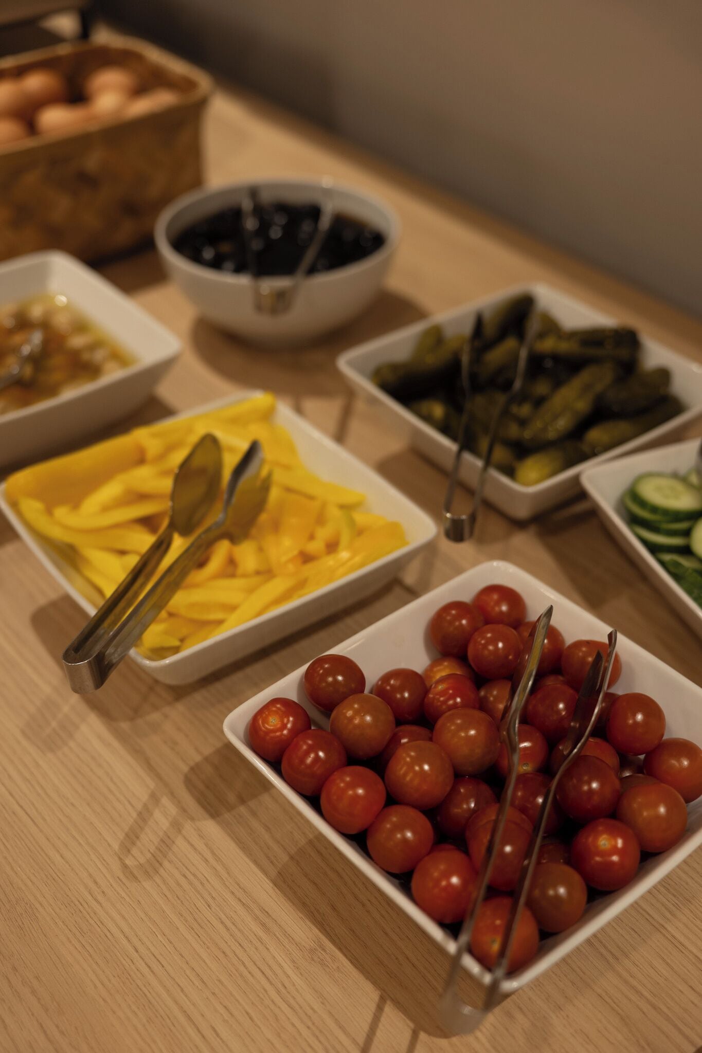 Ein Buffet mit verschiedenen Speisen, darunter eine Schüssel mit Kirschtomaten, eine Portion Pommes Frites und eine Dose Essiggurken.