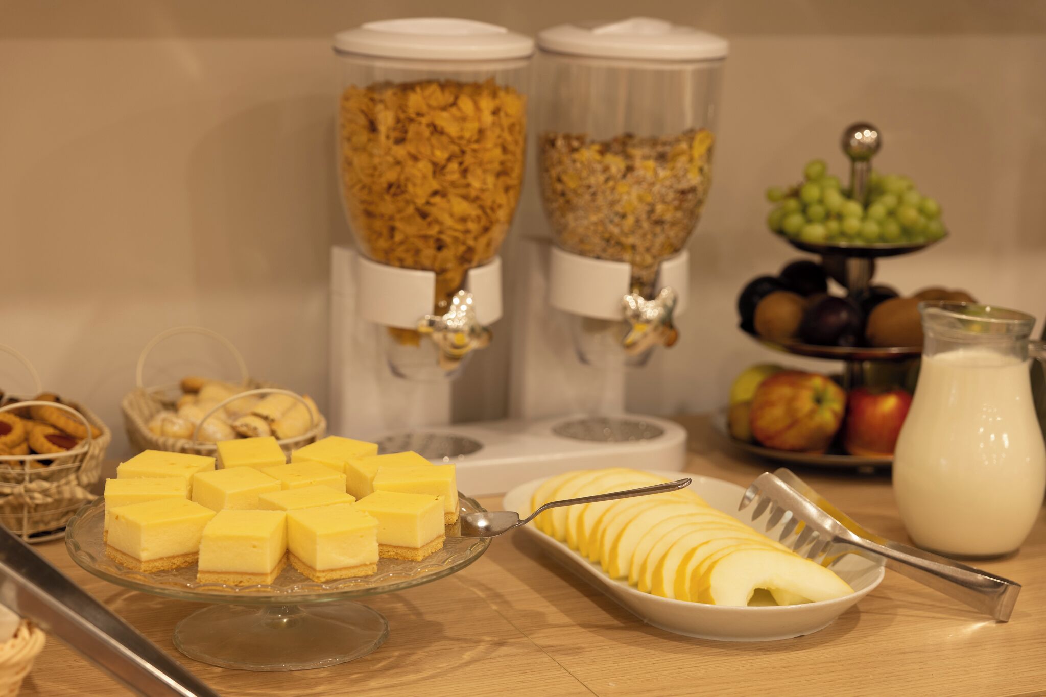 A buffet with various food items including a tray of yellow cheese, sliced apples, and a milk jug.