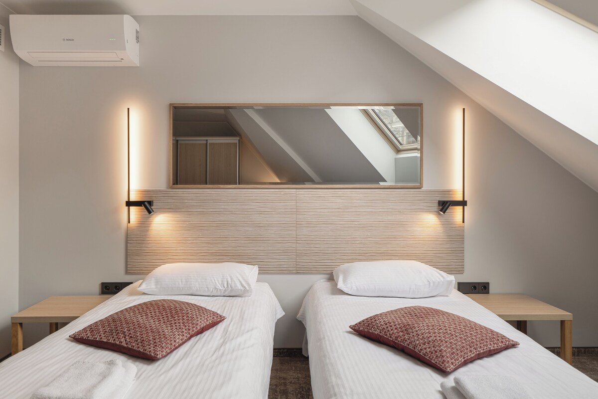 A hotel room with two beds, a skylight, a mirror, and a wall-mounted air conditioner.