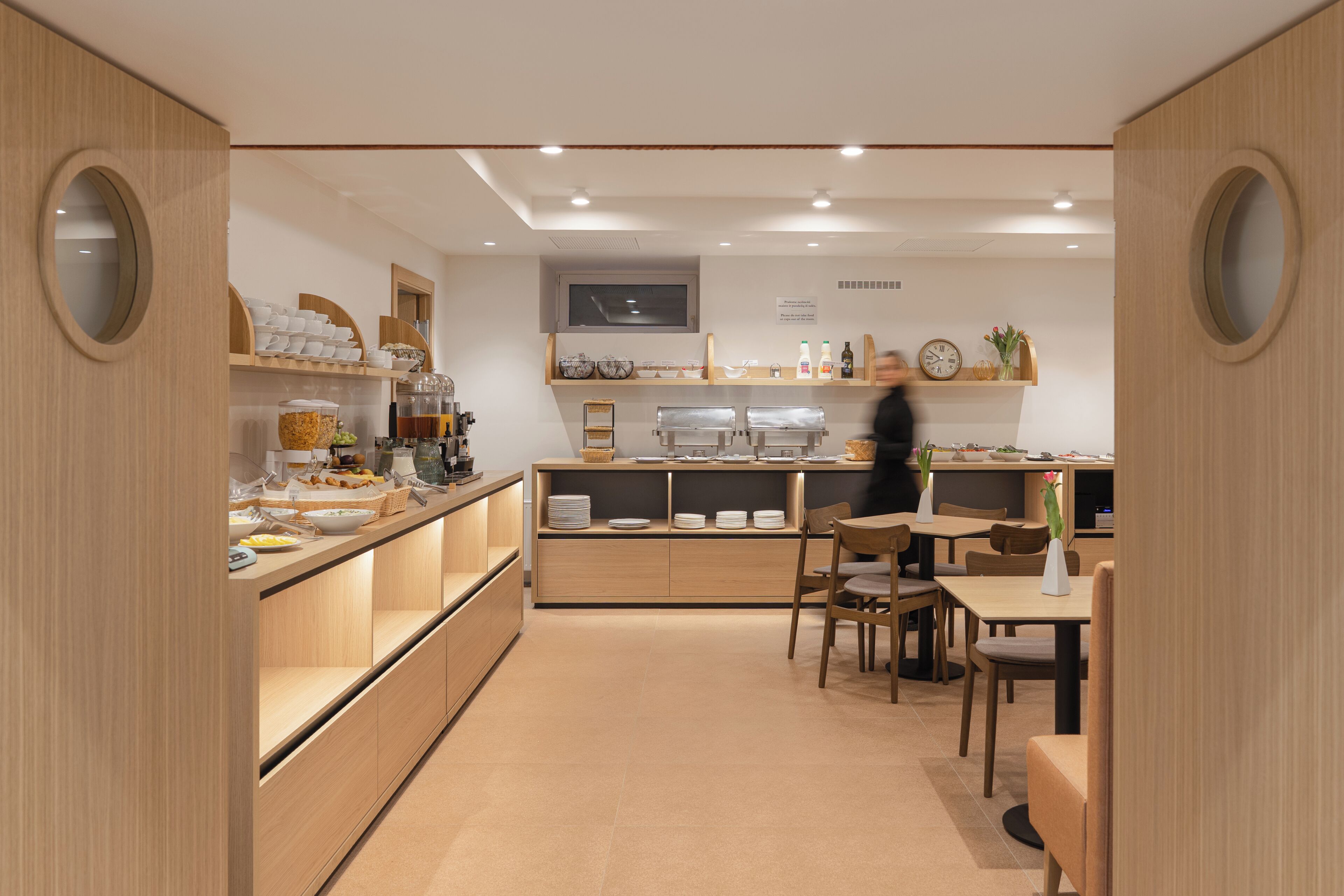 A modern cafe with wooden furniture, a counter with food items, and a seating area.