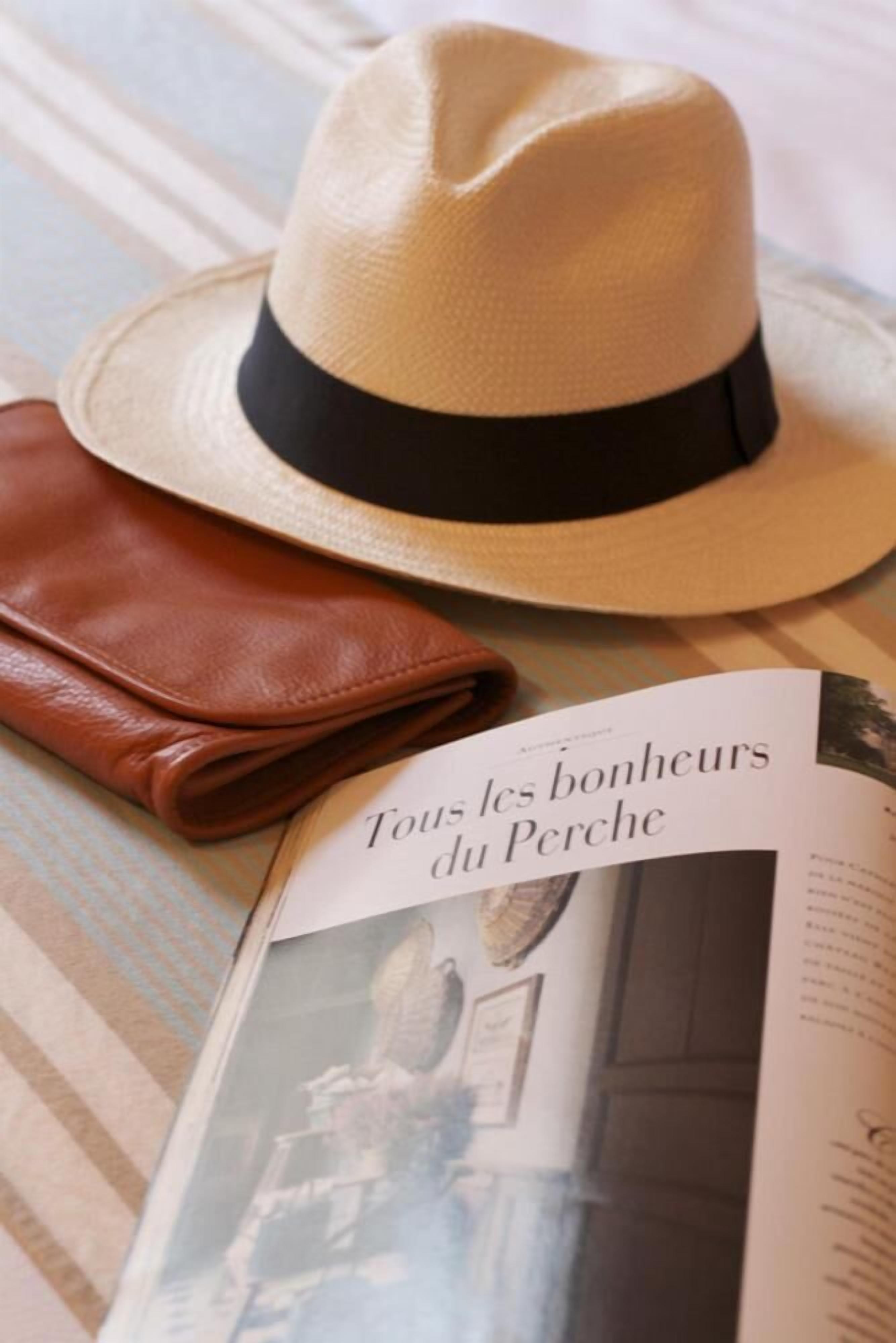 Un chapeau de paille avec un ruban noir, un article en cuir marron et un magazine intitulé « Tous les bonheurs du Perche ».