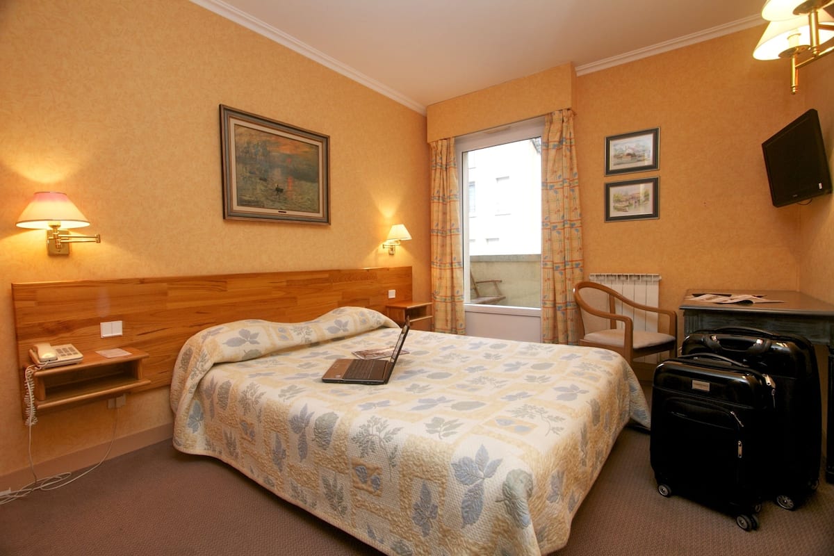 Habitación de hotel con cama, escritorio, silla, lámpara, un cuadro y televisor.