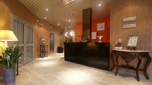 A reception area with a wooden floor, a reception desk, a wall-mounted sign, and a potted plant. - Logis Hotel Sully (Nogent-le-Rotrou)