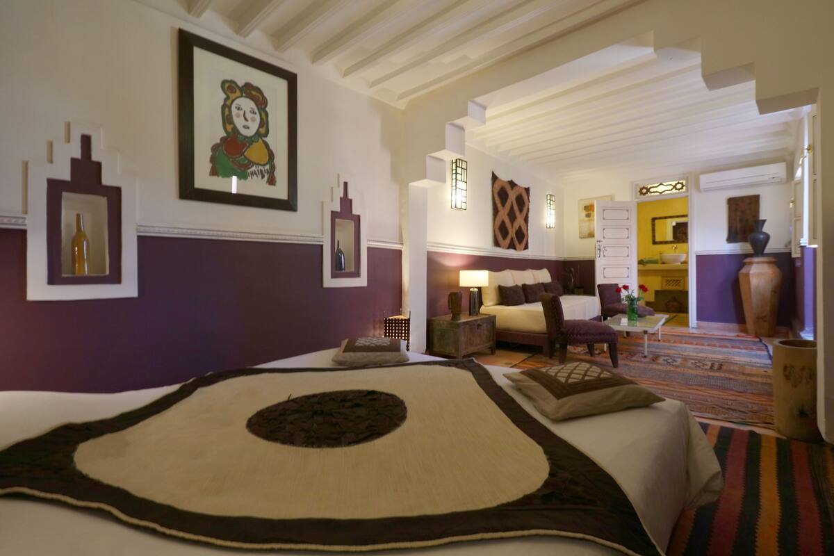 Ein Hotelzimmer mit einem großen Bett, einer Sitzecke mit einer Couch und Sesseln, einem kleinen Tisch und einem dekorativen Teppich.