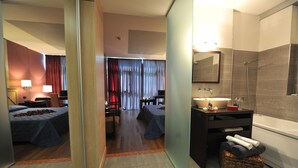 A hotel room with two beds, a sitting area, a bathroom with a bathtub, and a large mirror. - Hotel Antares (Villafranca di Verona)