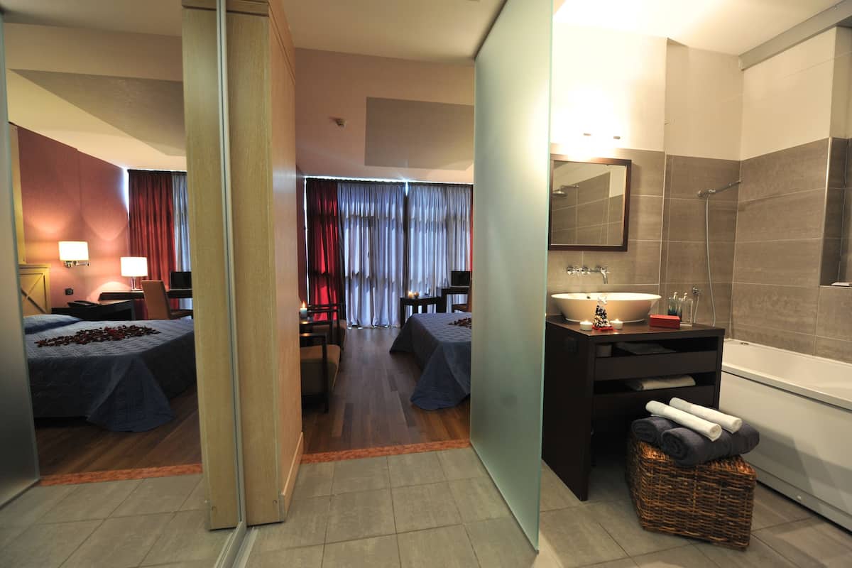 A hotel room with two beds, a sitting area, a bathroom with a bathtub, and a large mirror.