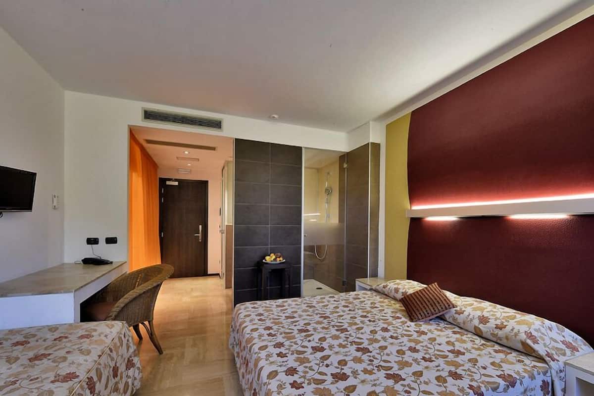 A hotel room with two beds, a desk, a TV, and a bathroom.