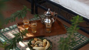 A bed with white bedding and a red pillow, a tray with food and drinks, and a metal teapot on a tiled table. - Riad Dar Nimbus (Marrakech)