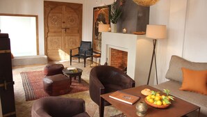 A living room with a fireplace, leather armchairs, a sofa, and a coffee table with a book and a bowl of fruit. - Riad Dar Nimbus (Marrakech)