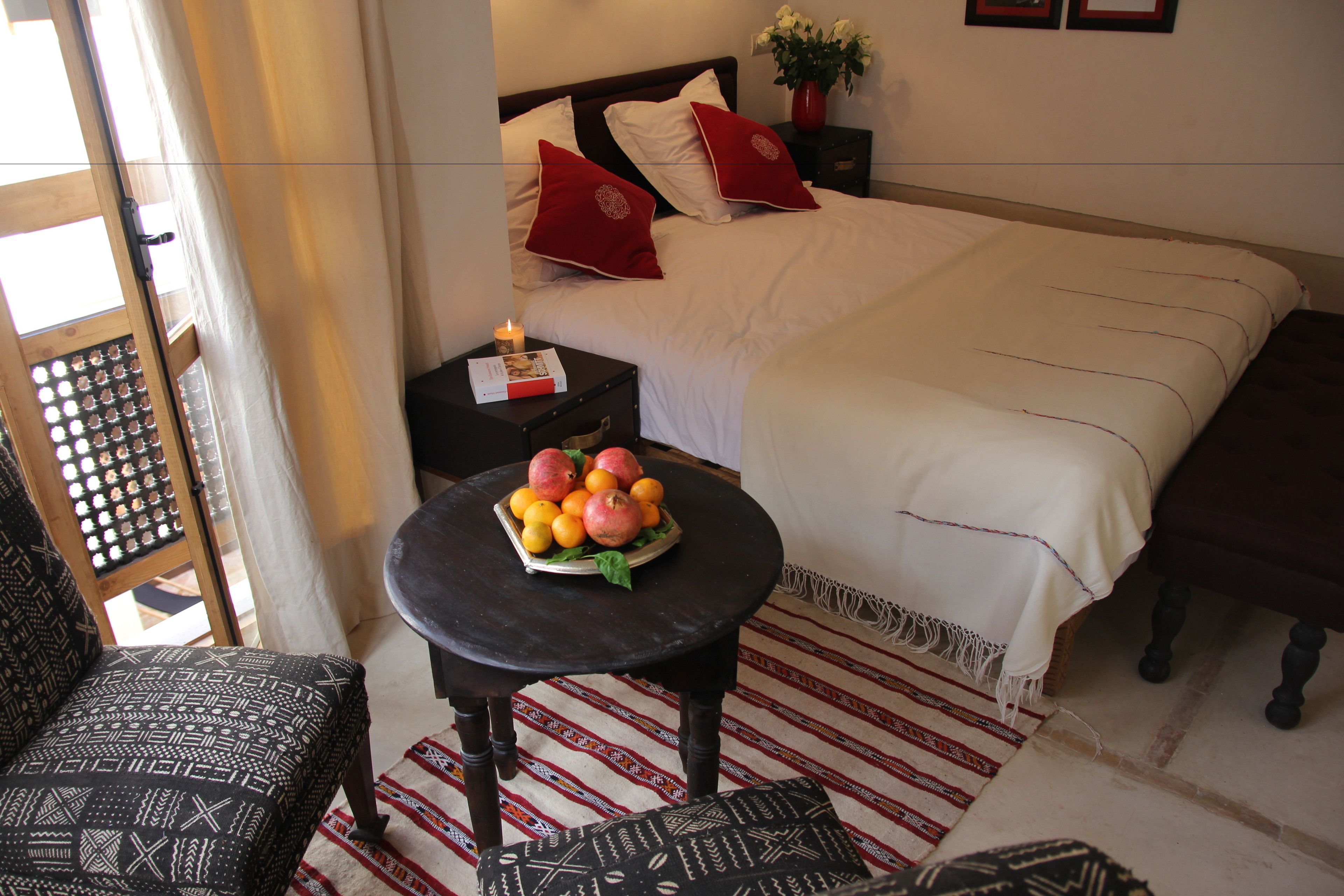 A neatly arranged bedroom with a bed, bedside table with a fruit bowl, a chair, and a patterned rug.