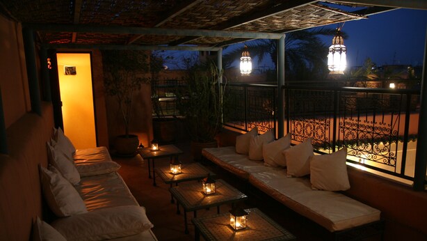 A dimly lit outdoor seating area with tables and a sofa, featuring lanterns and a view of a courtyard. - Riad Dar Nimbus (Marrakech)