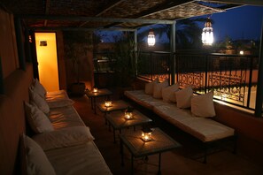 Un área de estar al aire libre con poca luz, con mesas y un sofá, con faroles y vistas a un patio.