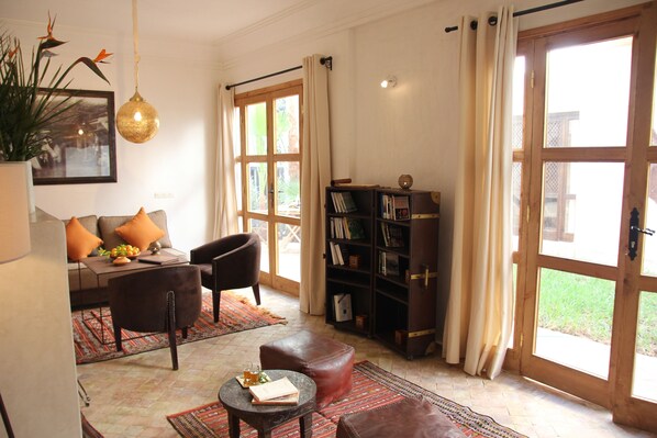 A living room with a sofa, chairs, a coffee table, a bookshelf, and a large window with curtains.