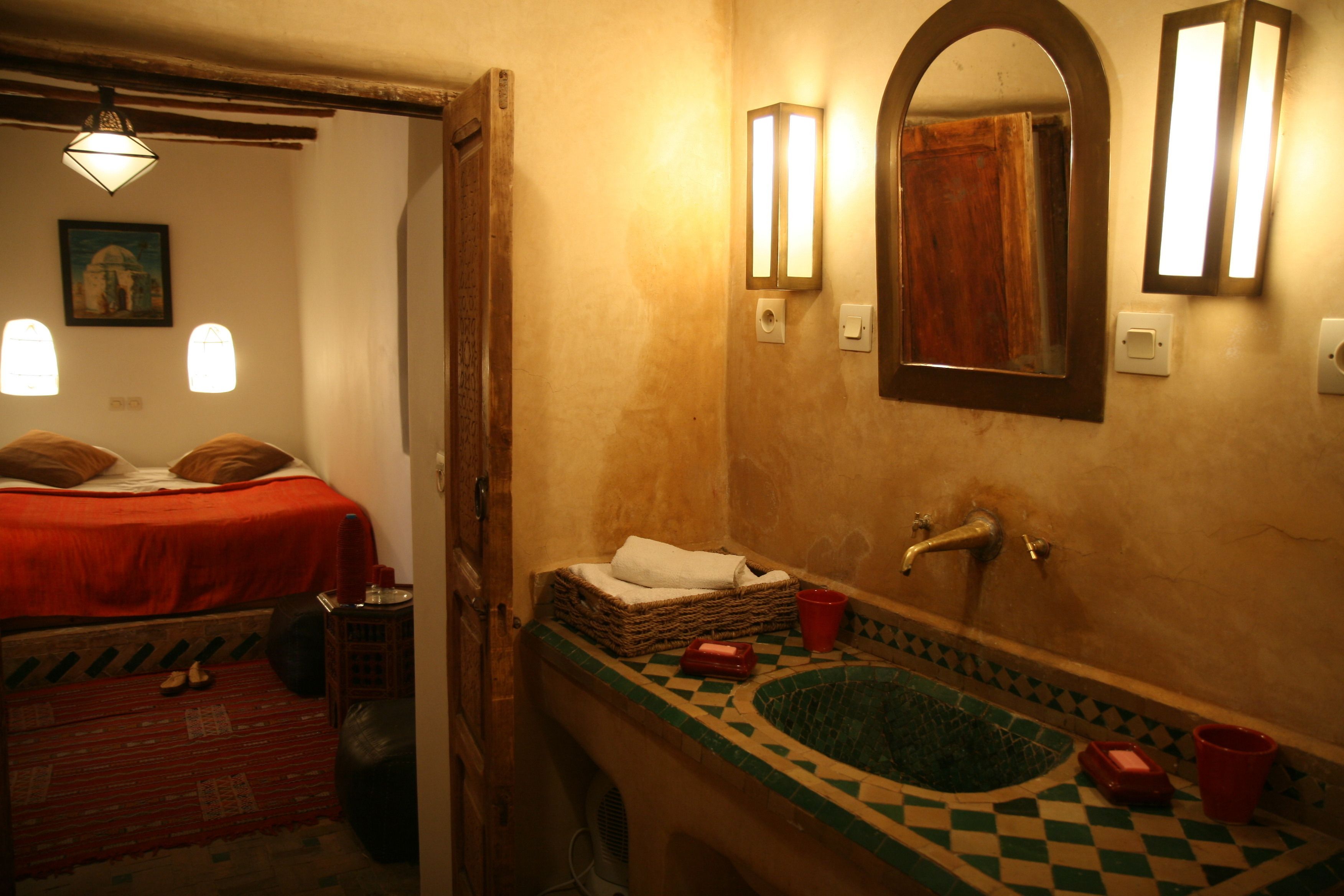 Una habitación con una cama, una mesita, un espejo, un lavabo y una ventana.