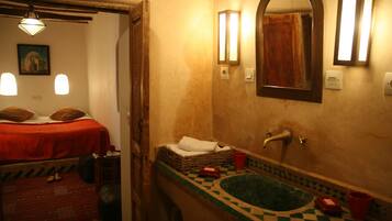 Una habitación con una cama, una mesita, un espejo, un lavabo y una ventana.