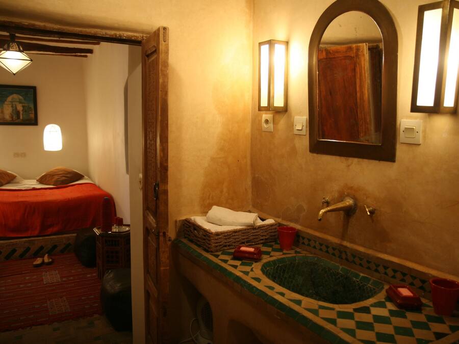 Una habitación con una cama, una mesita, un espejo, un lavabo y una ventana.