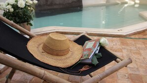 A lounge chair with a straw hat and a book, near a pool with a potted plant of white flowers. - Riad Dar Nimbus (Marrakech)
