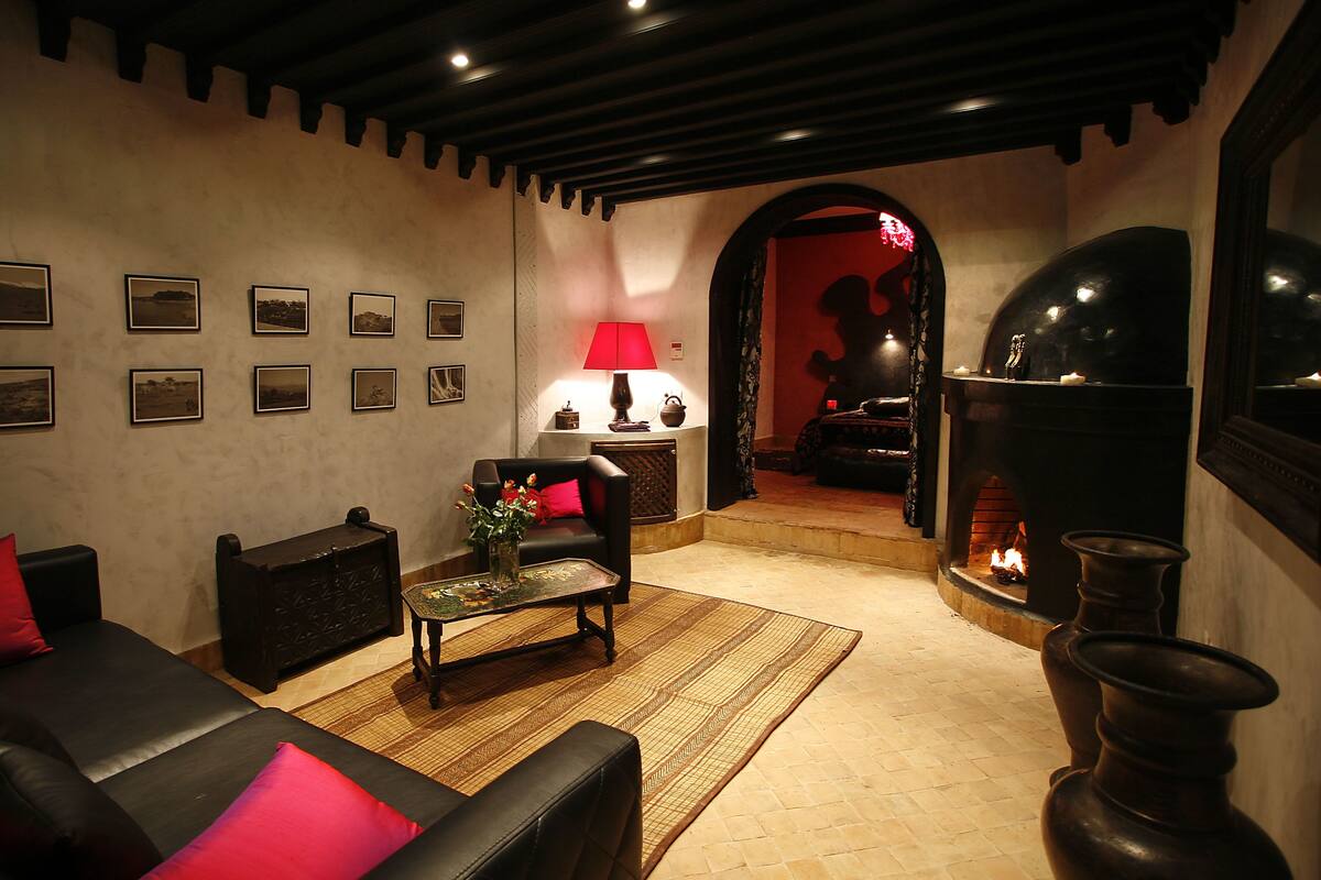 A cozy living room with a fireplace, a coffee table, and a sofa with red cushions.