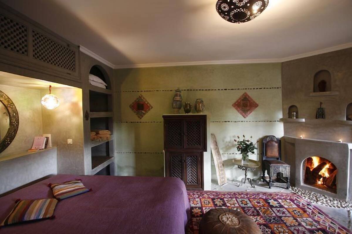 A room with a bed, a fireplace, shelves, and decorative items.