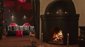 Una habitación acogedora con chimenea, una cama con almohadas rojas y una zona de estar con cojines de cuero.