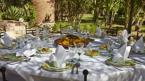 Un área de comedor al aire libre con una mesa dispuesta para una comida, rodeada de follaje y una estructura de piedra.