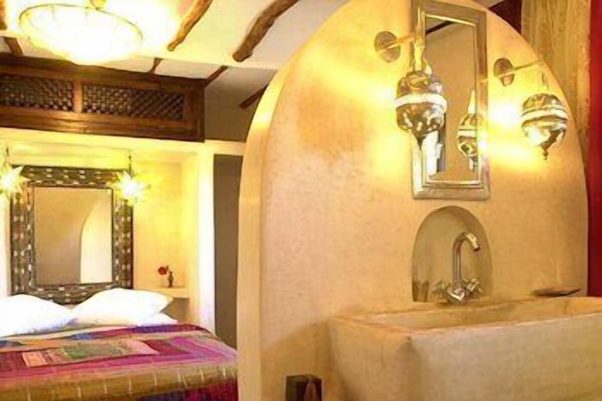 A bedroom with a large bed, a bedside table, a mirror, and a wall-mounted sink.