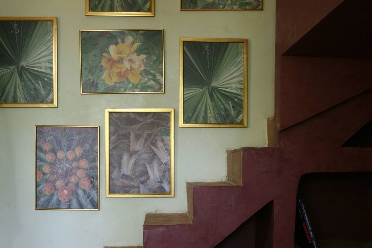A hotel room with a staircase, a bed with red bedding, and several framed floral paintings on the wall.