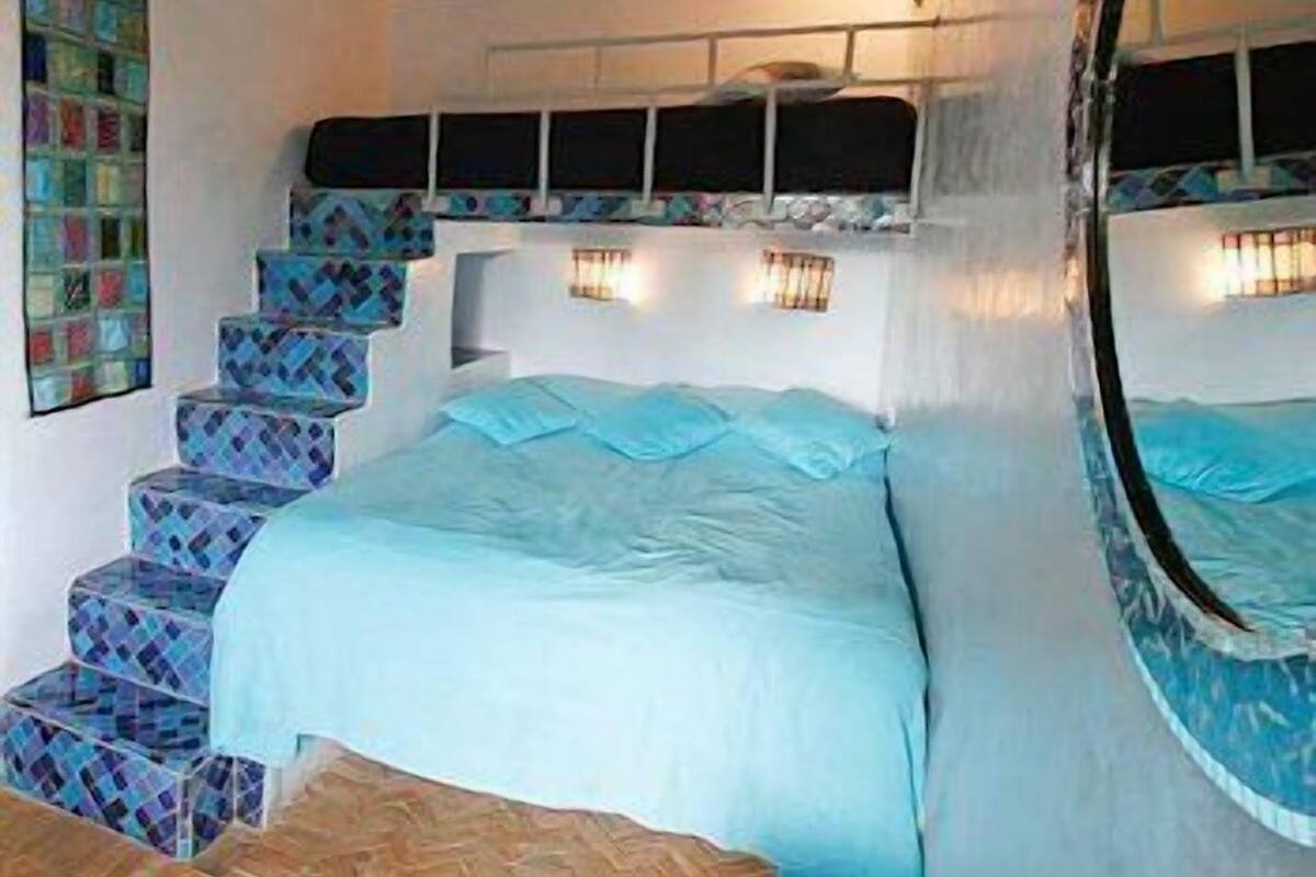 A bedroom with a bed, a staircase with patterned steps, and a wall-mounted light fixture.