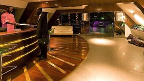 A modern lobby with a curved reception desk, a seating area with a sofa and a dog statue, and a staircase leading to an upper level. - Hotel Lagon 2 (Dakar)
