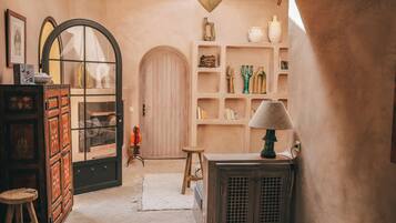 Un interior acogedor con una puerta de madera, un taburete pequeño, un mueble y estantes con objetos decorativos.
