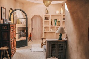 A cozy interior with a wooden door, a small stool, a cabinet, and shelves with decorative items.