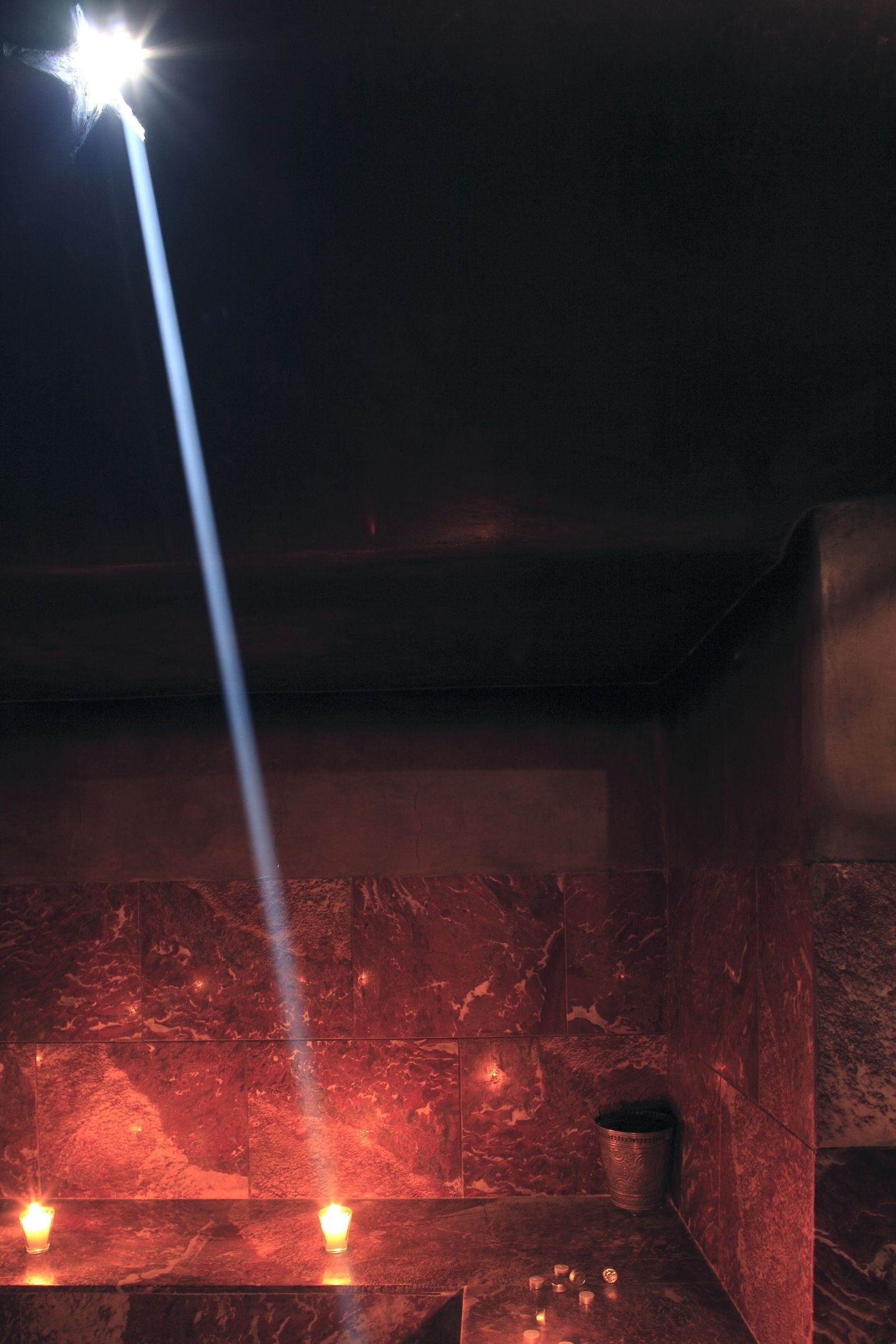 A dimly lit room with a single bright light source, a marble wall, and a small metal container on the counter.
