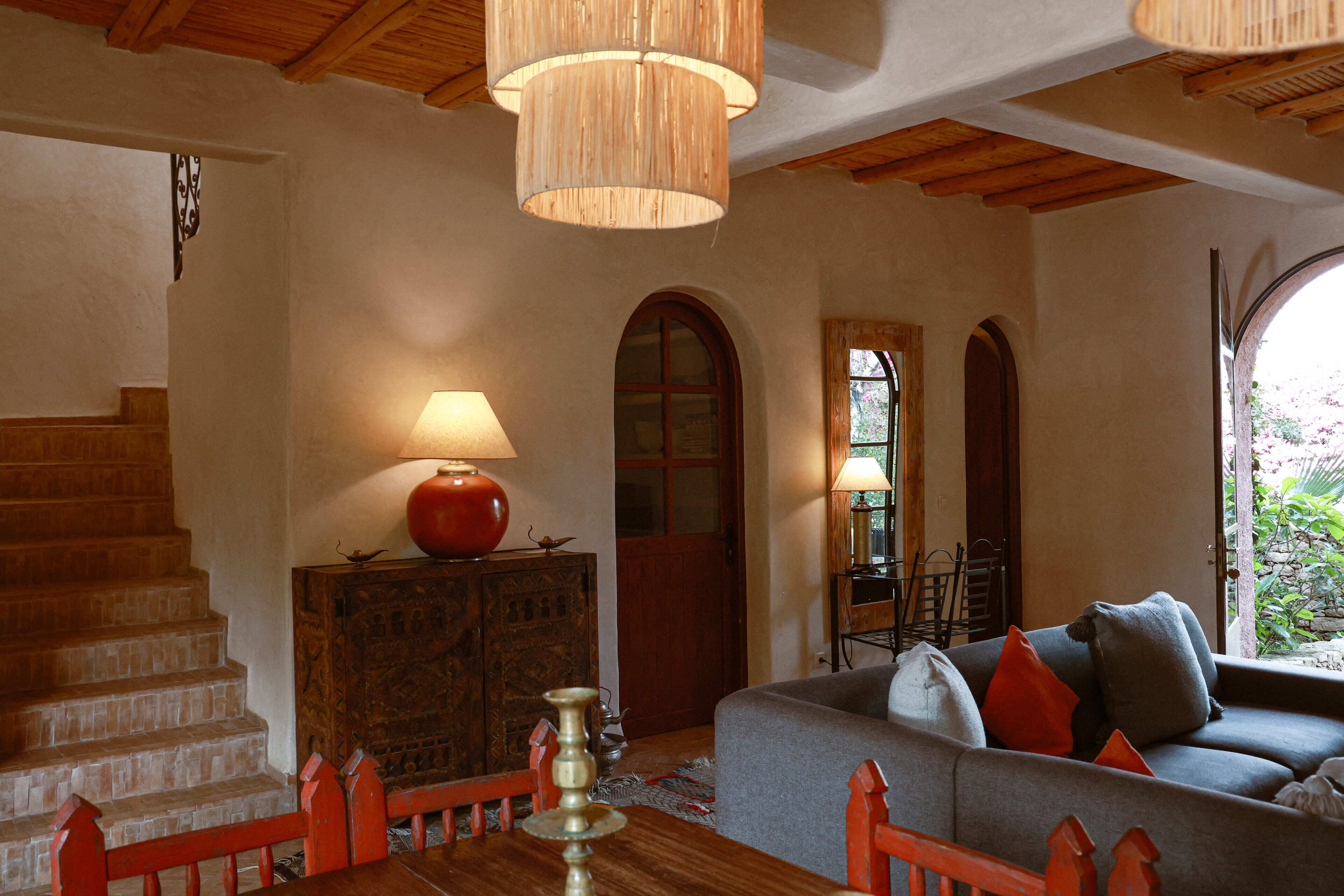 Une pièce avec un escalier, un canapé, une table avec une lampe et une vue à travers une fenêtre en arc de cercle.
