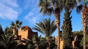 A pool with clear water reflecting palm trees and a building with a dome. - Le Jardin Des Douars (Aguerd)