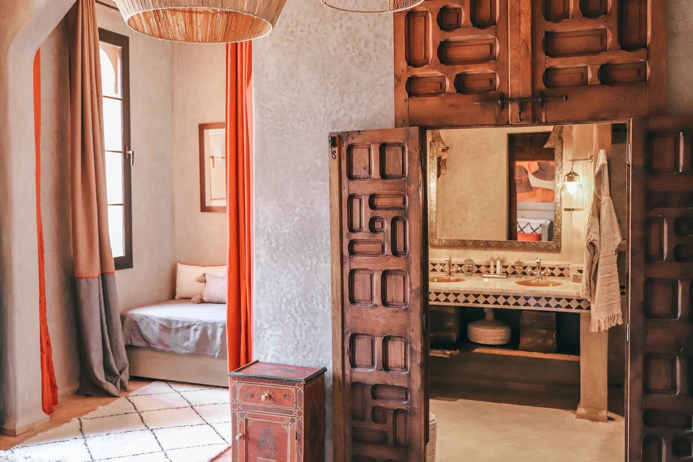 A room with a bed, a wooden door, a mirror, and a sink.