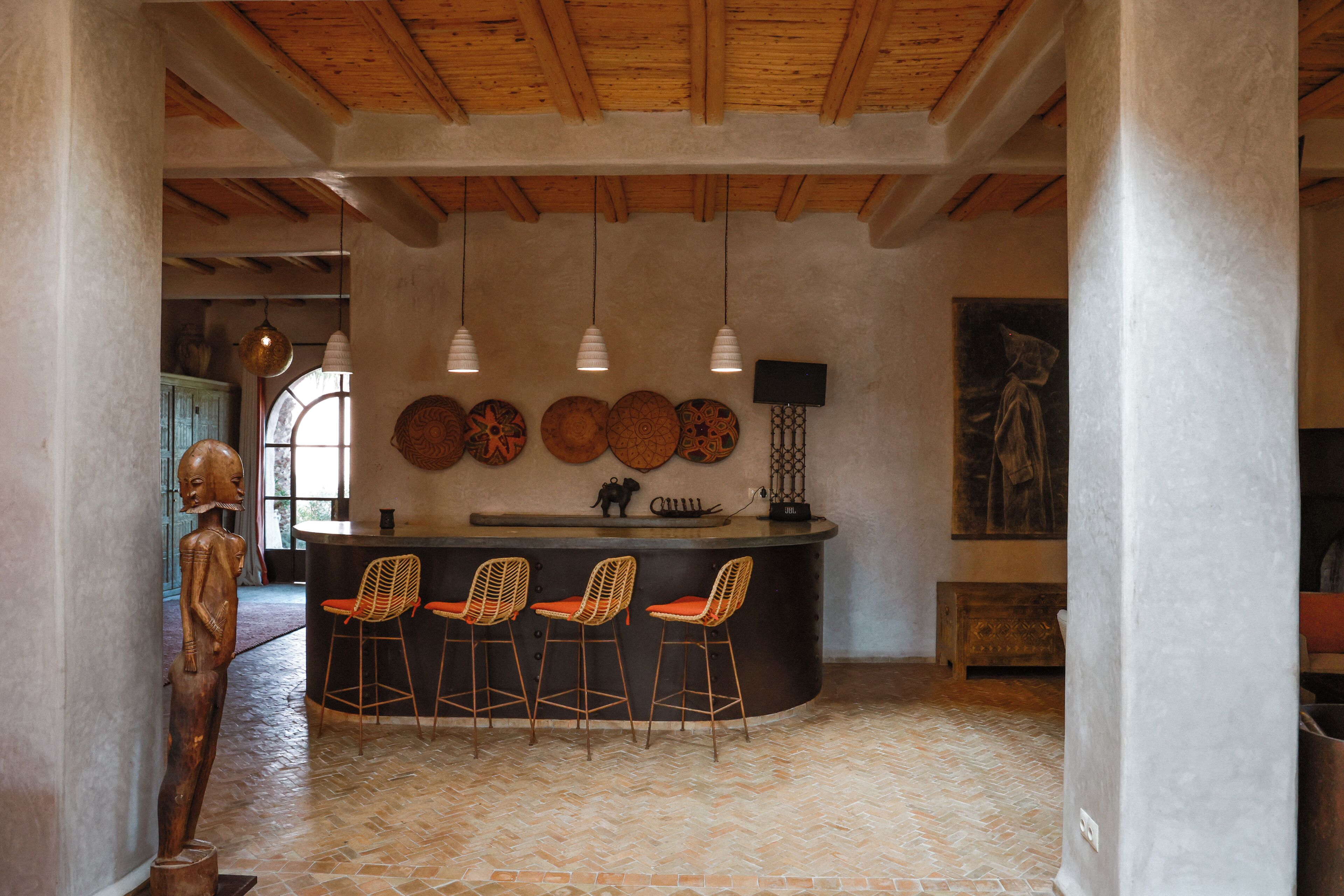 A bar area with a herringbone floor pattern, a counter with stools, pendant lighting, and wall decor.