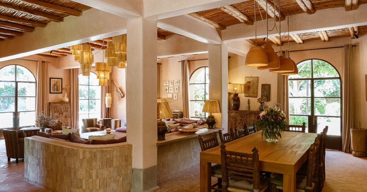 A spacious dining area with a wooden table and chairs, large windows with natural light, and hanging pendant lights.