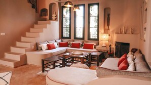 A cozy living room with a staircase, a sofa set, a dining table, and large windows. - Le Jardin Des Douars (Aguerd)